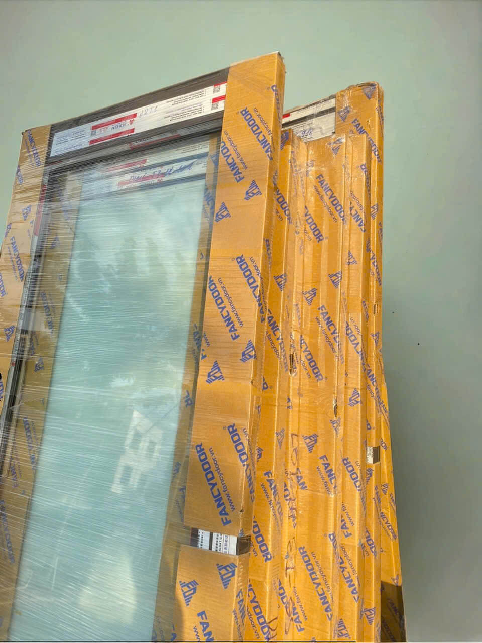 Cửa nhôm kính Fancydoor mới, còn nguyên bao bì, dựng cạnh tường chuẩn bị lắp đặt